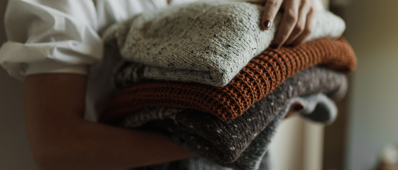 Ein Stapel gefalteter Strickpullover wird aus dem Schrank genommen